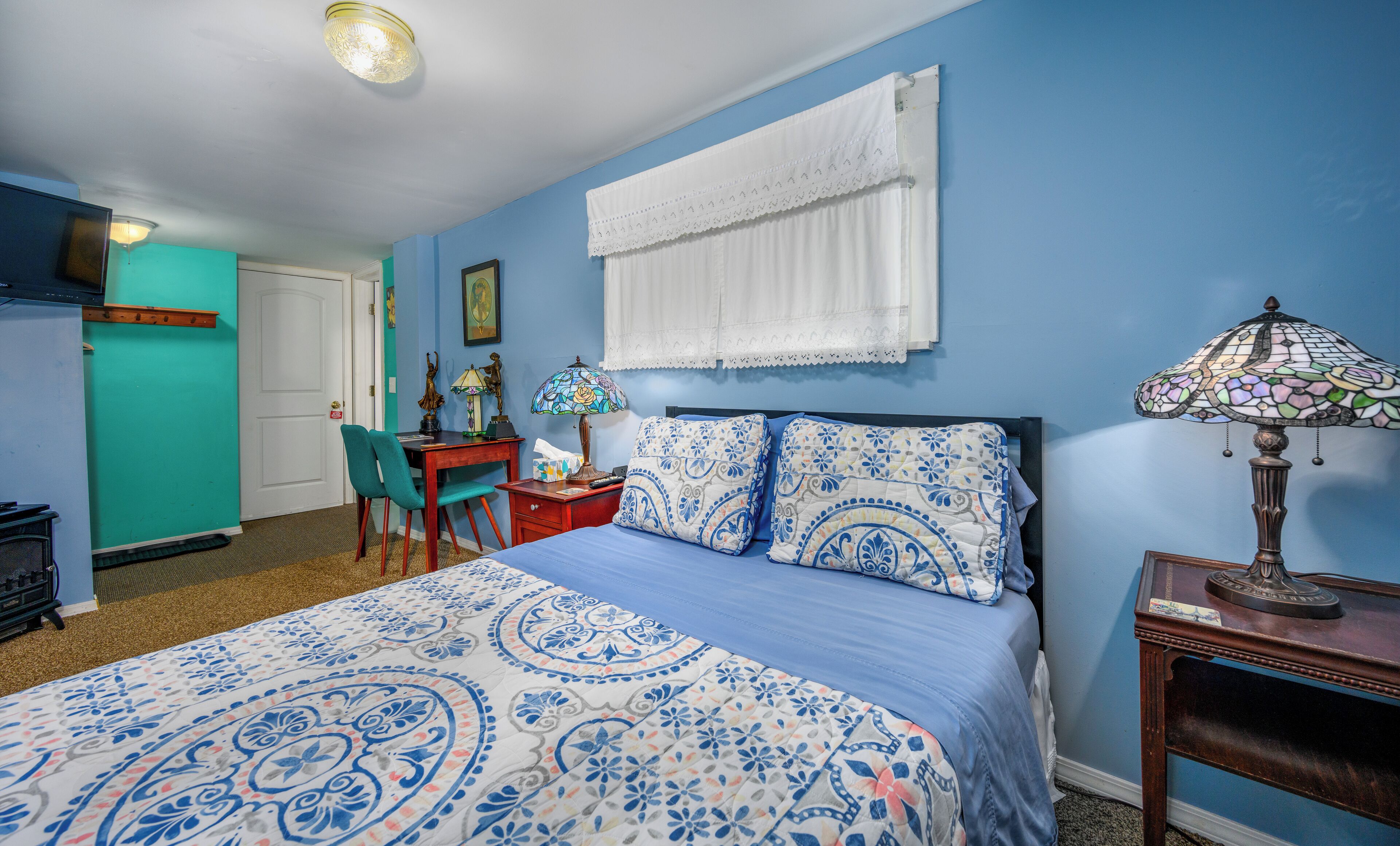 A bedroom with a bed, a desk, a chair, and a lamp.