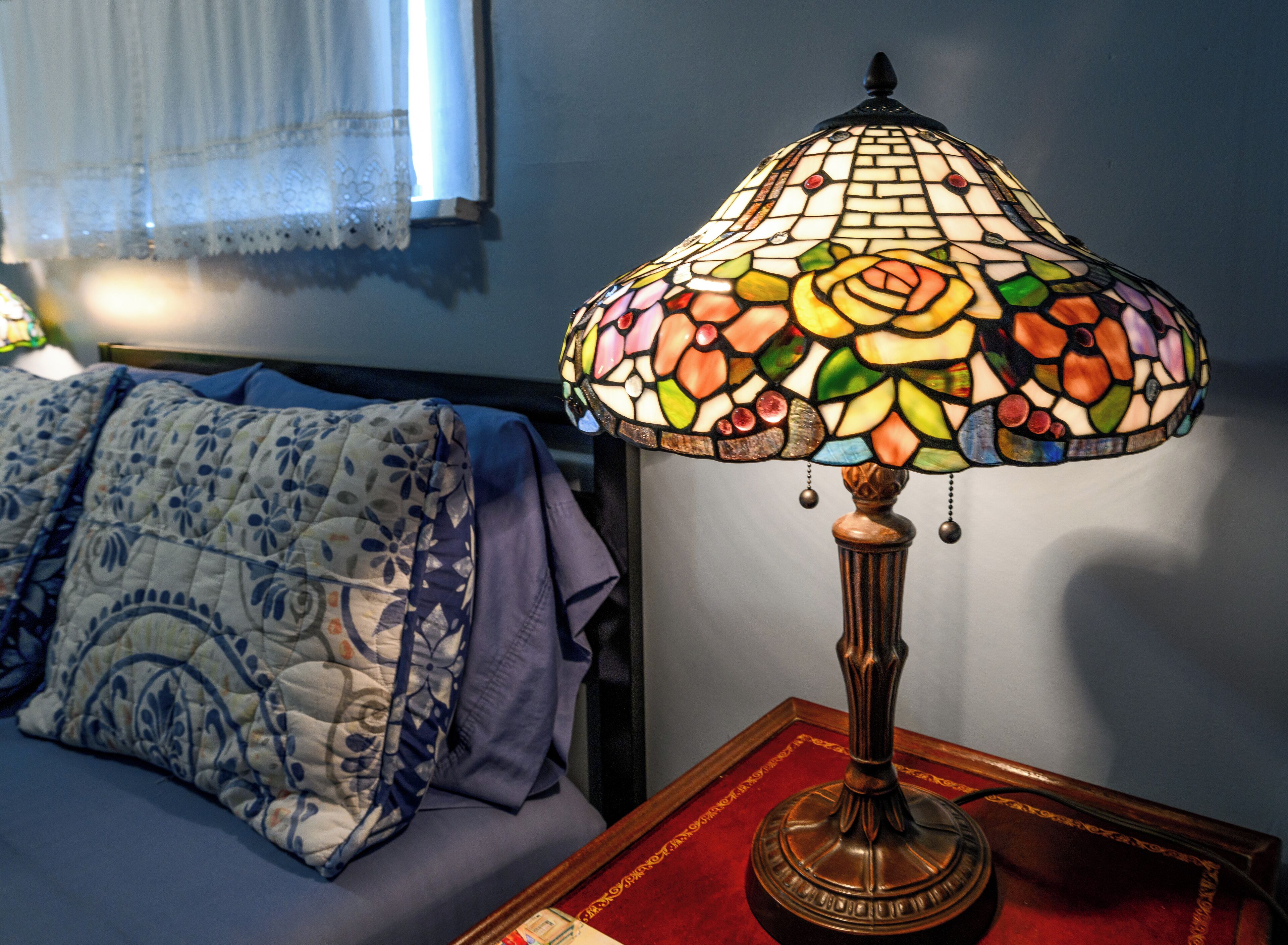 Een kamer met een bed, een nachtkastje met een lamp en een raam met gordijnen.