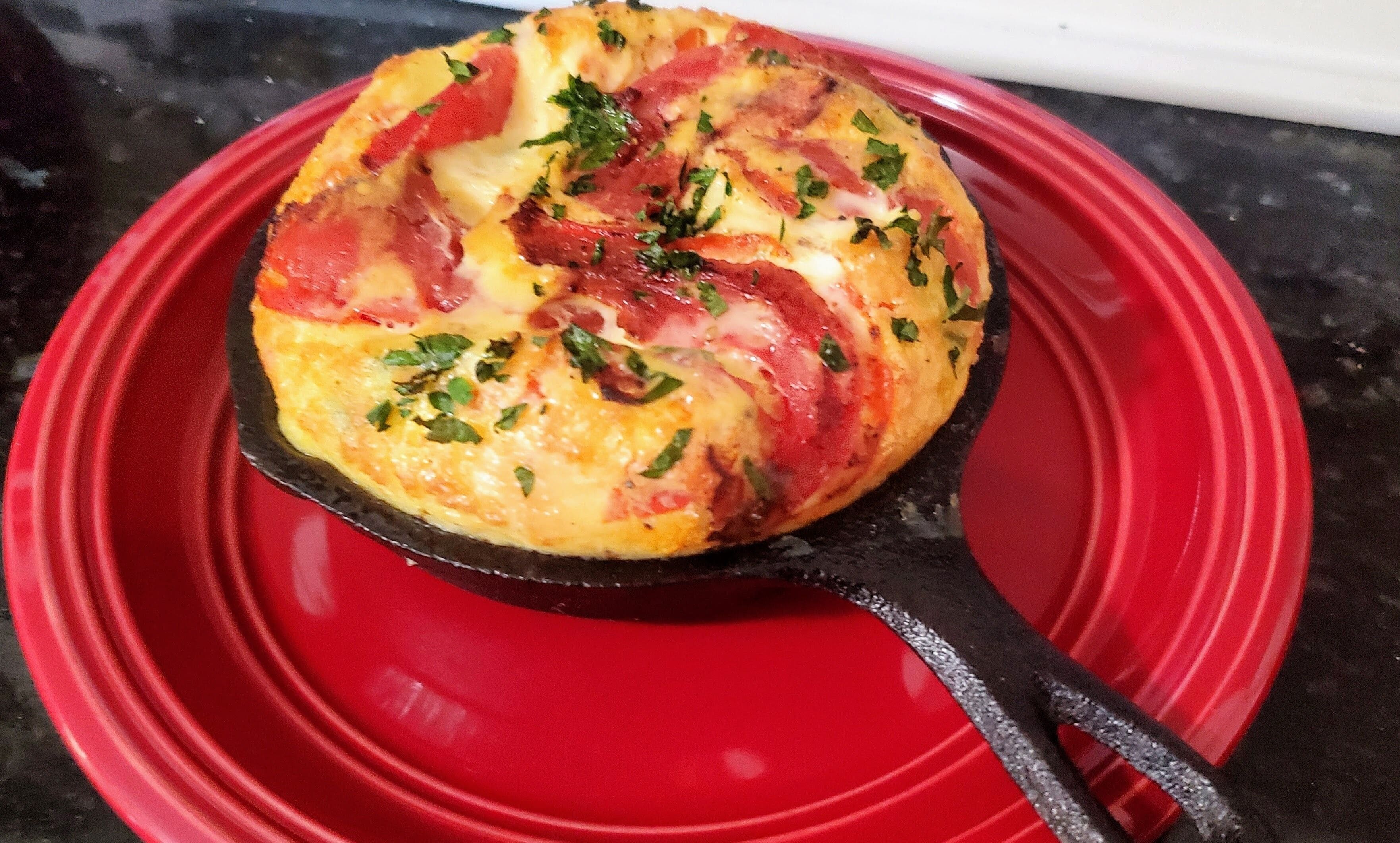 A red plate with a frittata on a black spatula.