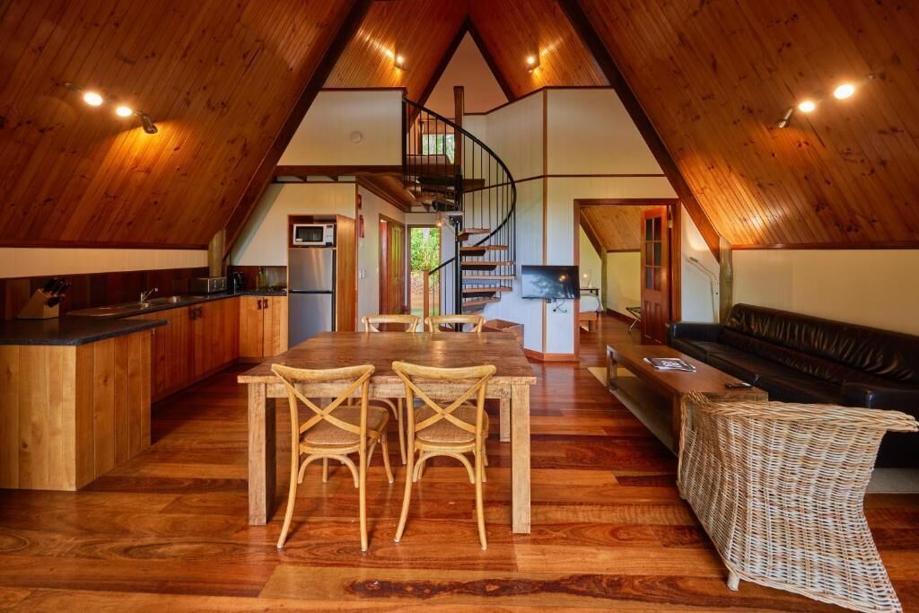 Un loft espacioso con techo alto, un área de comedor central con sillas, un sofá y una escalera que lleva a un nivel superior.