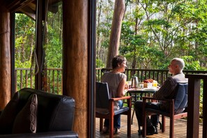 Une terrasse en bois avec deux chaises et une table, donnant sur une zone boisée.