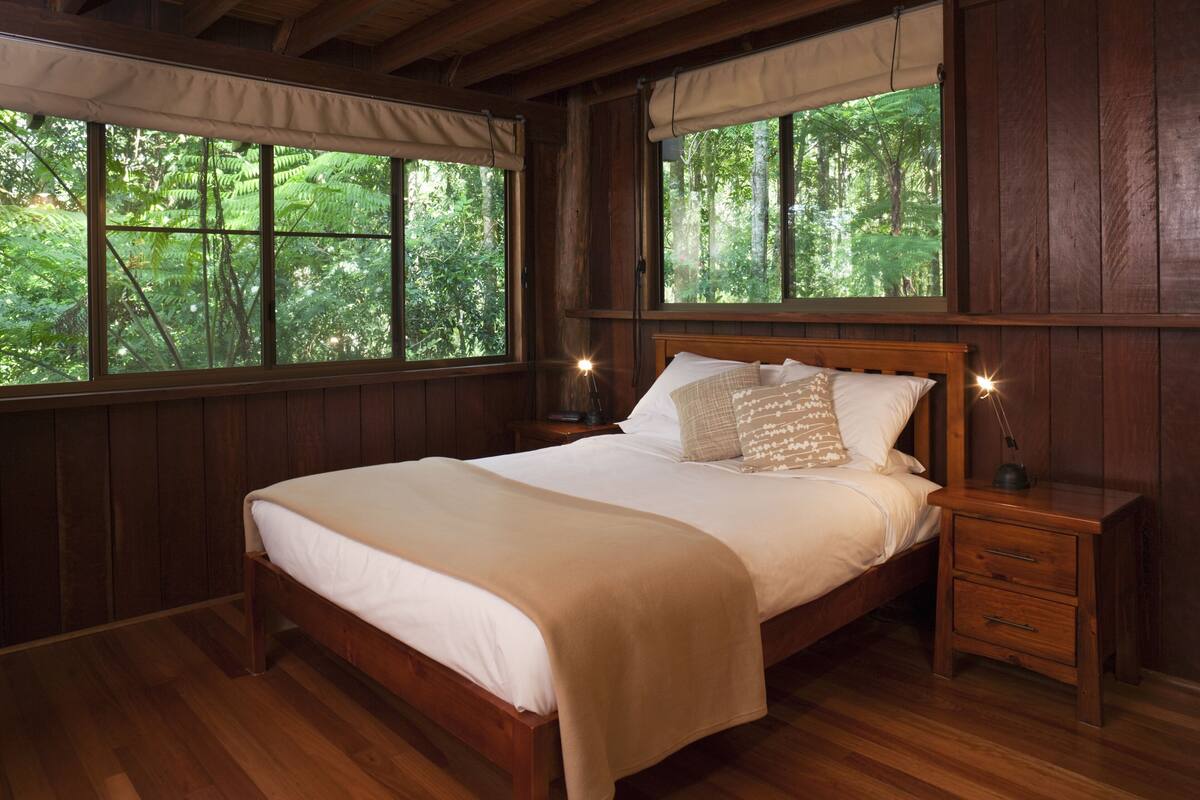 Ein Schlafzimmer aus Holz mit einem großen Bett, zwei Nachttischen und Fenstern mit Vorhängen.