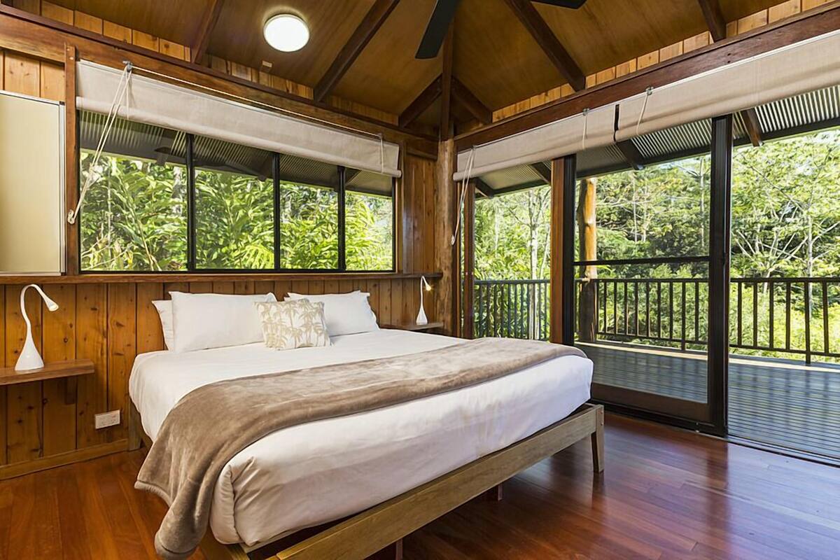 Ein Schlafzimmer aus Holz mit einem großen Bett, einem Nachttisch und einem Fenster mit Blick auf einen Balkon.