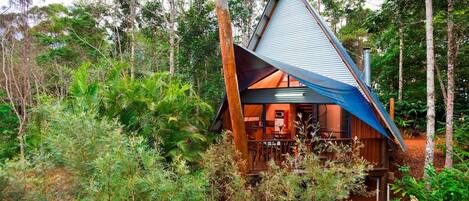 Una cabaña moderna con forma triangular rodeada de bosque denso.