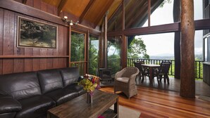 Ein Holzinterieur mit einer Ledersofa, einem Holztisch mit einer Vase, Korbstühlen und Blick durch große Fenster.
