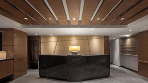 A reception area with a marble counter, wooden panel ceiling, and recessed lighting. - Green World Mai - NanJing (Taipei)