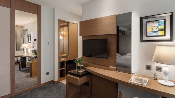 A modern hotel room with a wooden desk, a flat-screen TV, a large mirror, and a framed abstract painting. - Green World Mai - NanJing (Taipei)
