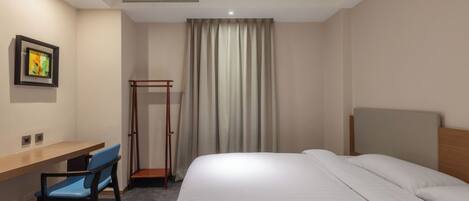 Une chambre d’hôtel avec un lit, un bureau, une chaise, un tableau au mur et une fenêtre avec des rideaux.
