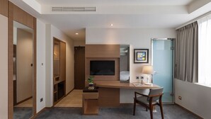 A hotel room with a wooden desk, a TV, a bed, a window with curtains, and a small plant. - Green World Mai - NanJing (Taipei)
