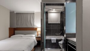 A hotel room with a bed, bedside table, lamp, and a glass-enclosed shower area with a sink and toilet. - Green World Mai - NanJing (Taipei)
