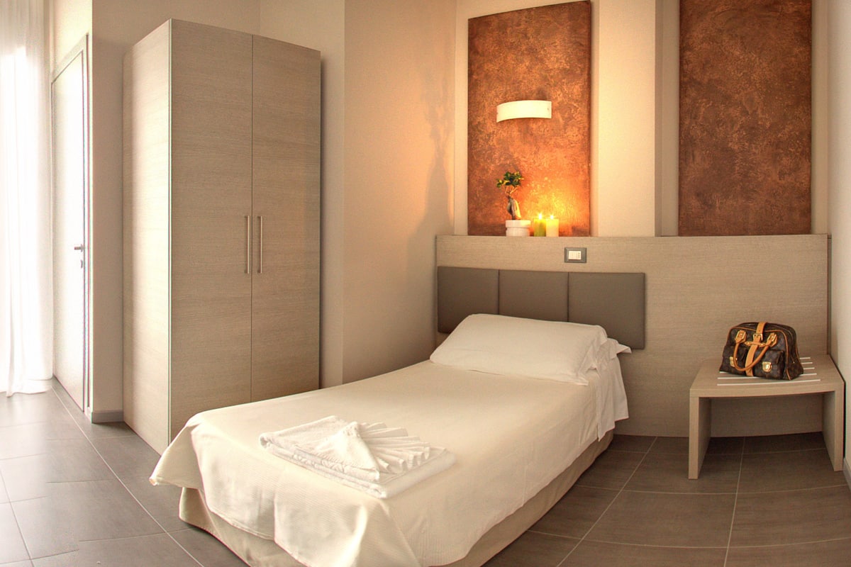 A hotel room with a bed, a nightstand, a wardrobe, and a wall-mounted light fixture.