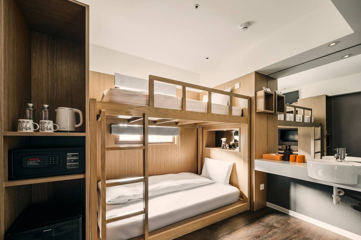 A compact room with bunk beds, a small kitchenette, a mirror, and a window.