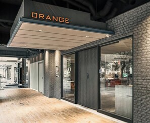 Un bâtiment moderne avec une enseigne « ORANGE » au-dessus de l’entrée, de grandes portes vitrées et un plancher en bois.