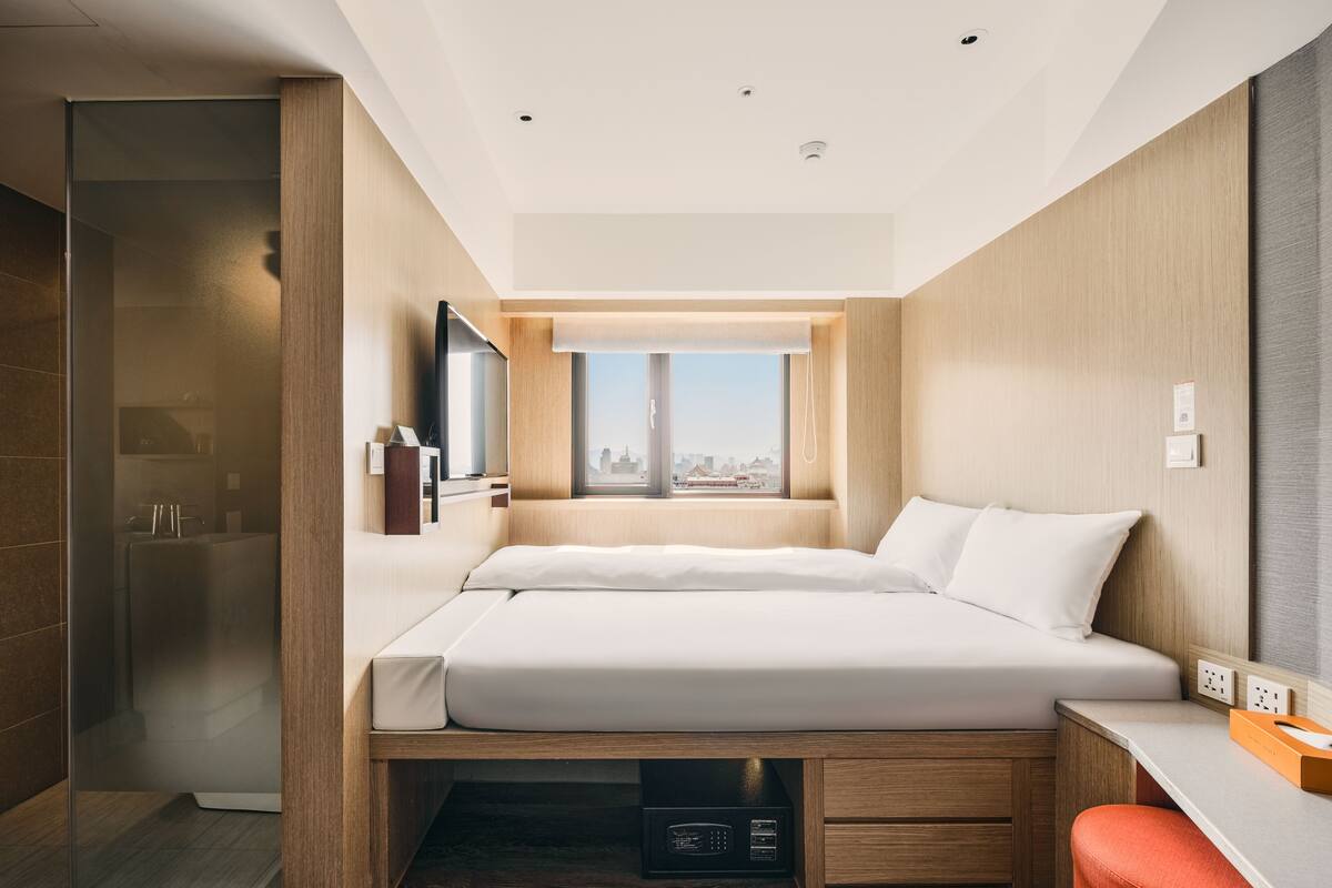 A modern hotel room with a bed, a desk, and a shower area.