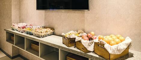 A buffet setup with various food items, a flat-screen TV mounted on the wall, and a tiled floor.