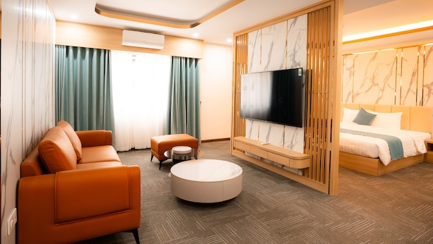 A modern hotel room with a sofa, round coffee table, and a bed with a TV. - Capital Garden Hotel (Hanoi)