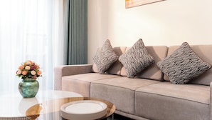 A modern living room with a beige sofa, patterned cushions, a glass coffee table, and a vase of flowers. - Capital Garden Hotel (Hanoi)