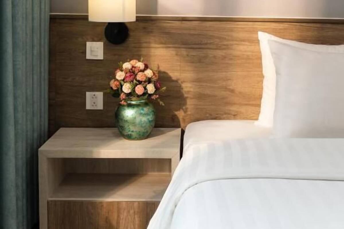 A hotel room with a wooden headboard, a bedside table with a vase of flowers, a lamp, and a bed with white bedding.