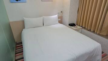A hotel room with a large bed, two pillows, a bedside table with a phone and a lamp, a striped rug, and two wall art pieces.