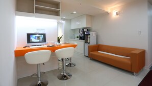 A modern waiting area with a reception desk, two bar stools, an orange sofa, and a kitchenette in the background. - Morwing Hotel Fuzhong (New Taipei City)
