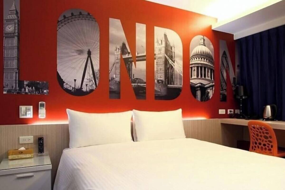 Une chambre d’hôtel avec une grande fresque murale représentant des monuments emblématiques de Londres, un lit, un bureau et une chaise.