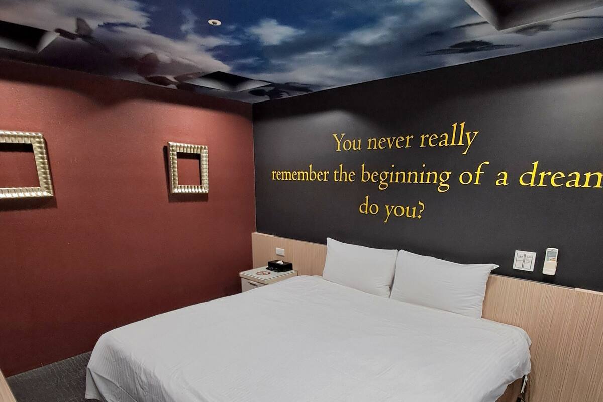 Une chambre d’hôtel avec un lit, une table de chevet, une horloge murale et une citation inspirante sur le mur.