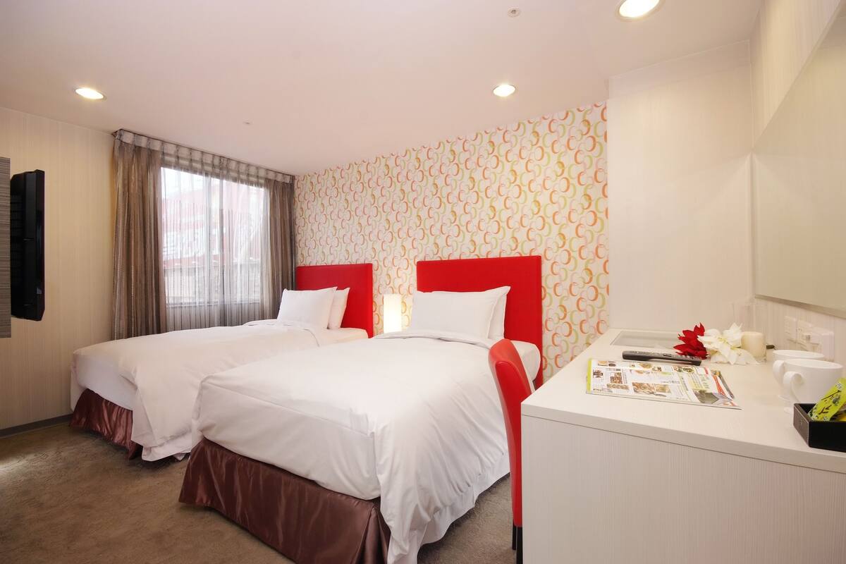 A hotel room with two beds, a desk, and a mirror.
