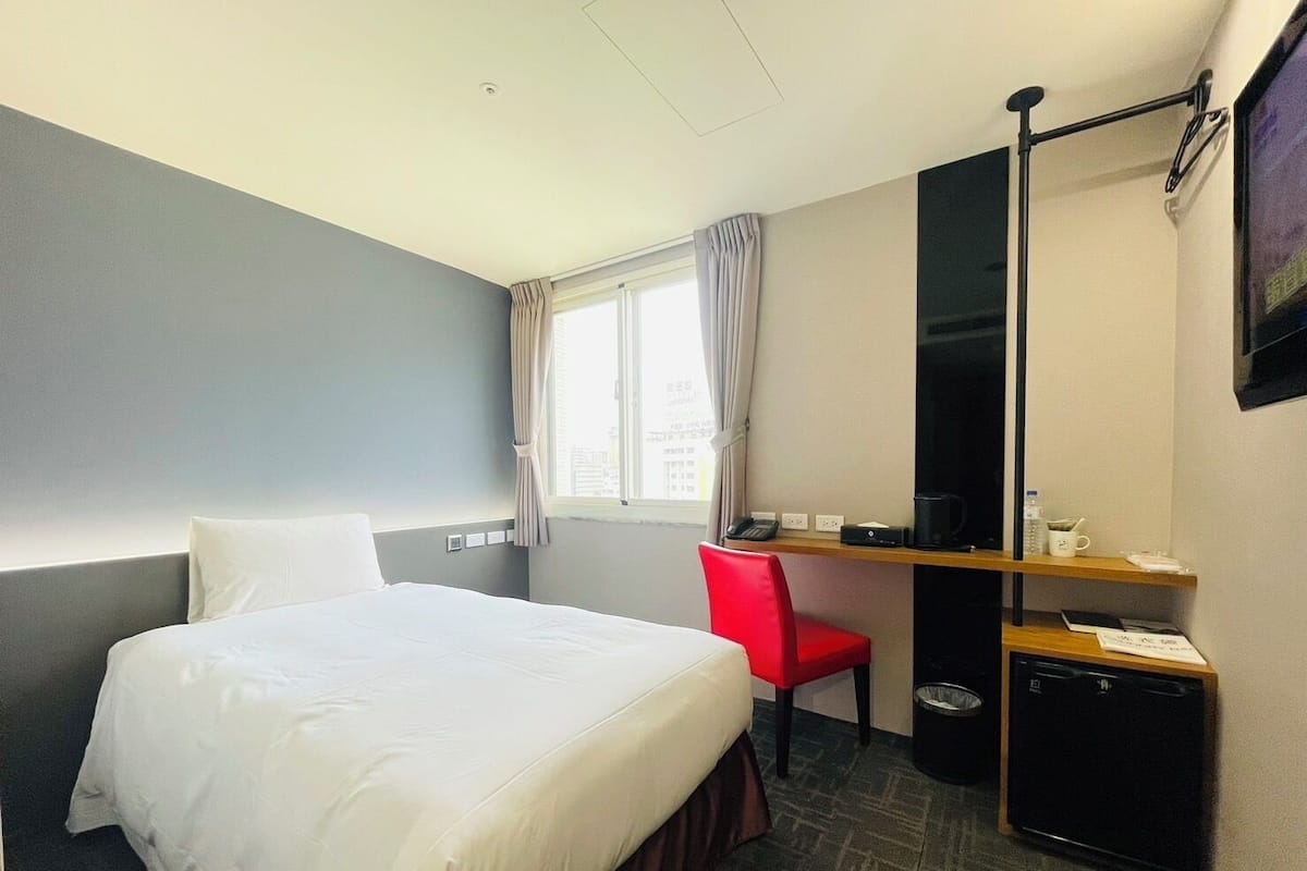 A hotel room with a bed, a desk with a chair, a TV, and a small kitchenette.