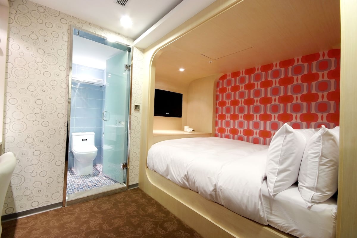 A hotel room with a bed, a toilet, and a shower area.