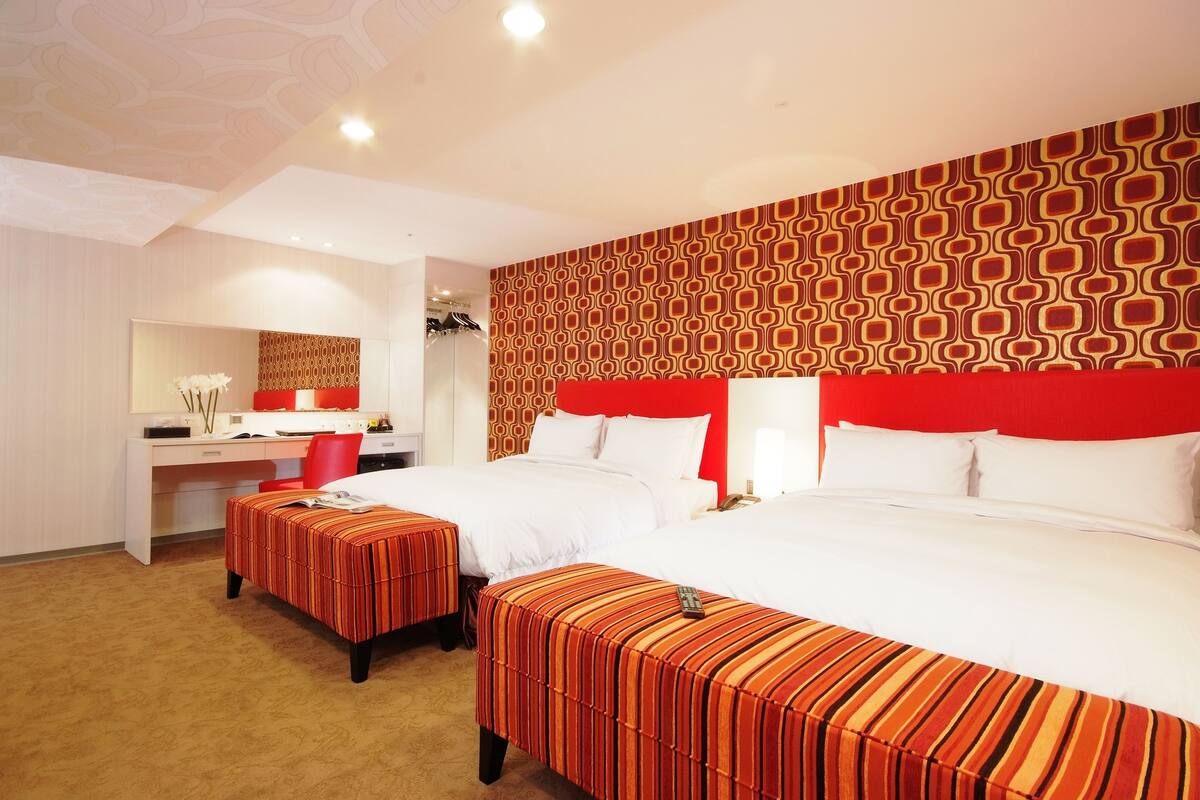 A hotel room with two beds, a desk, and a mirror.