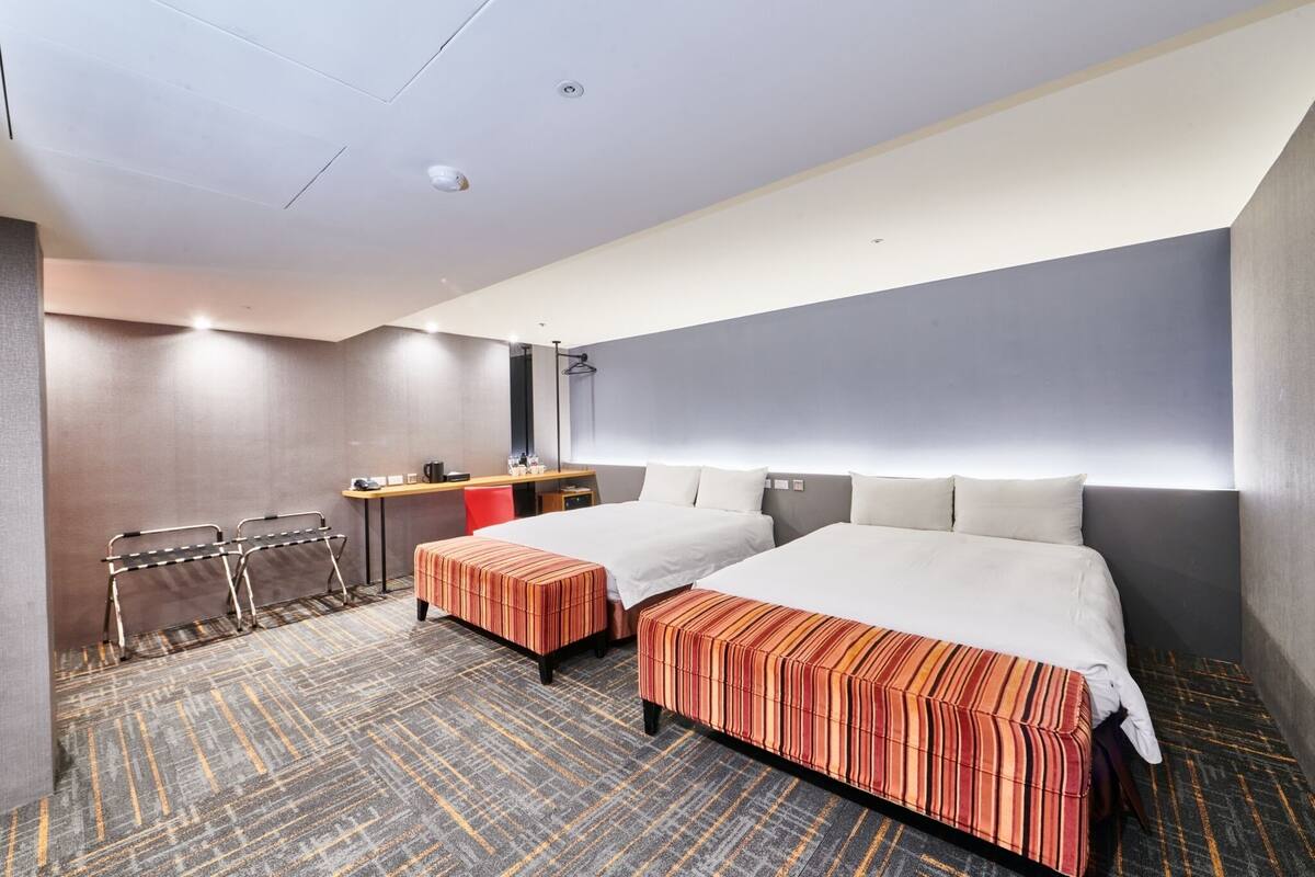 A hotel room with two beds, a desk, a chair, and a mirror.