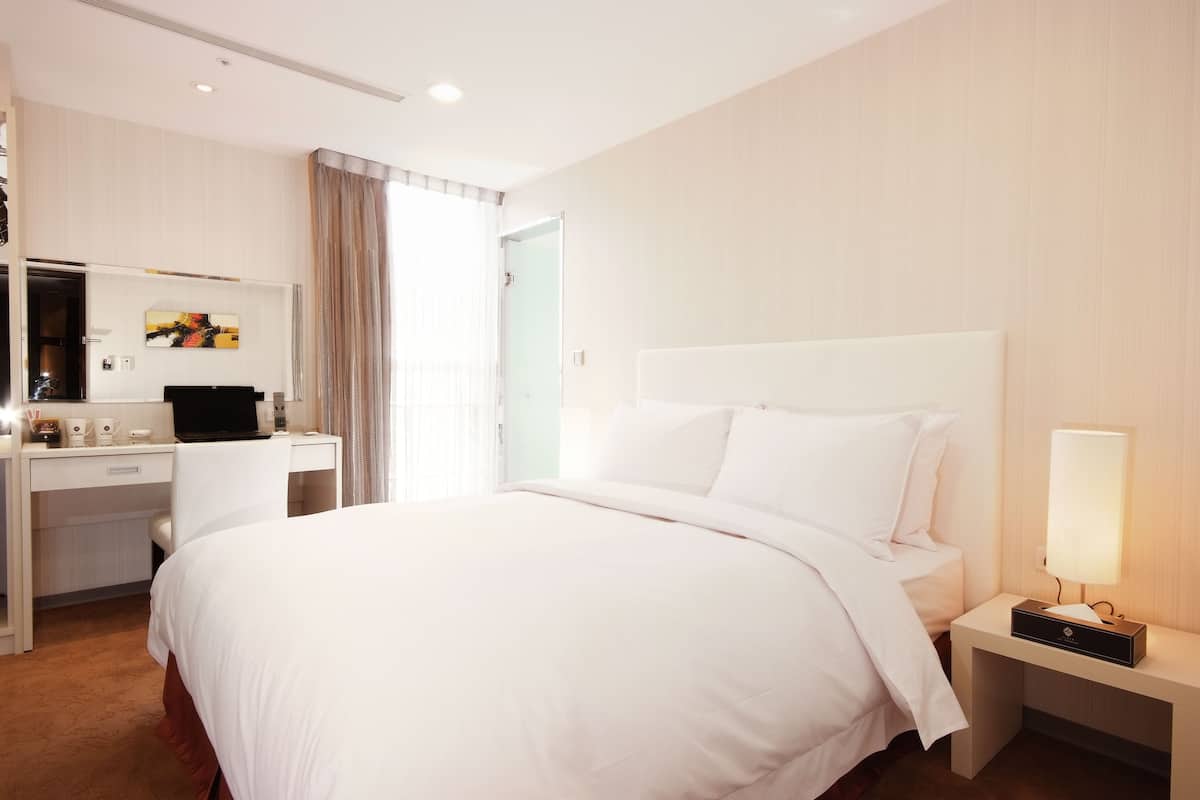 A hotel room with a large bed, a desk with a computer, a bedside lamp, and a mirror.