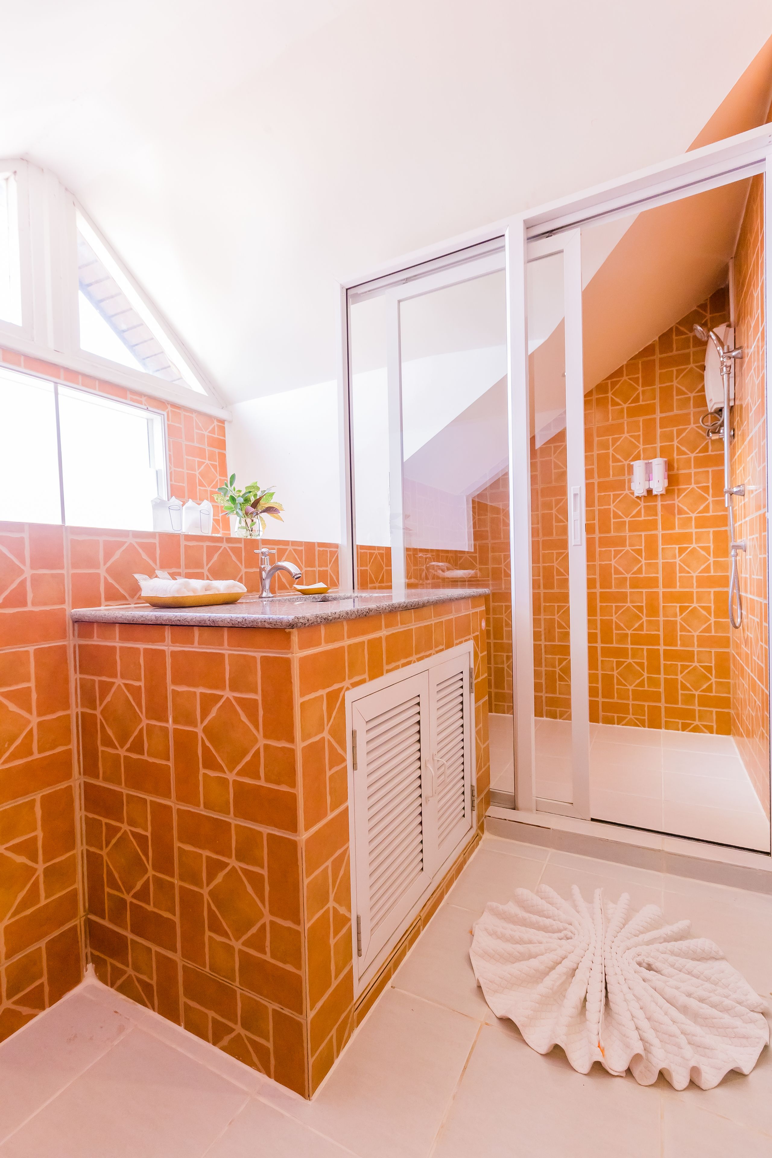 A bathroom with orange tiled walls, a white sink, and a shower area.