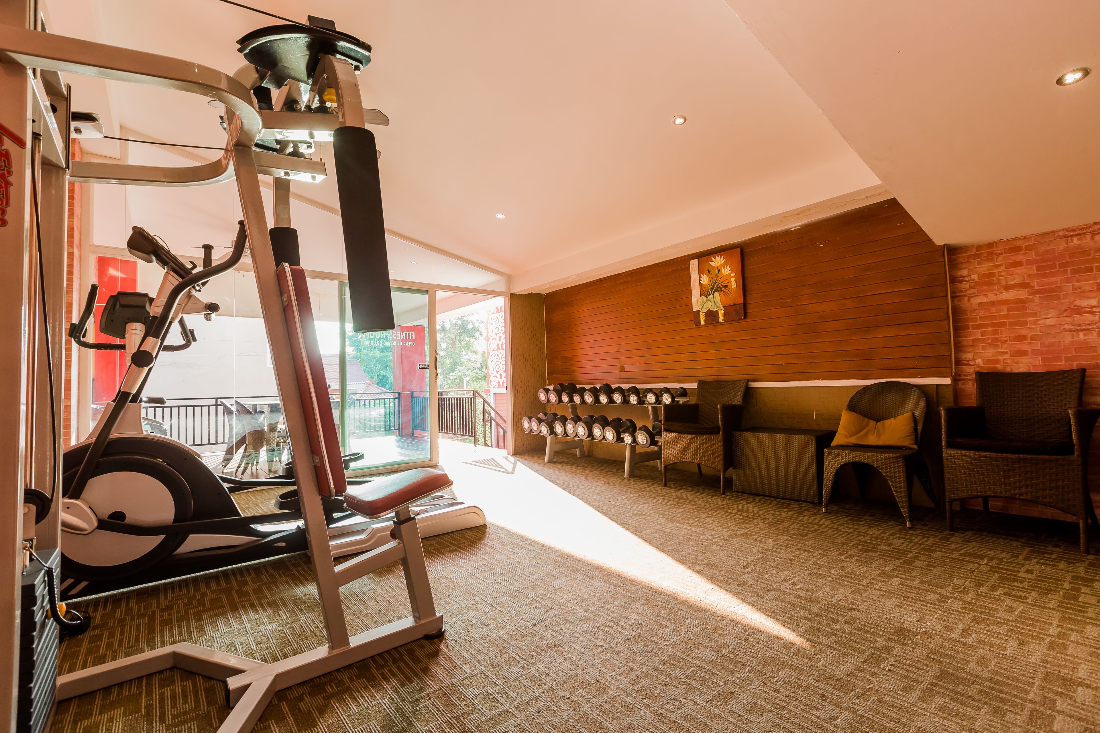Een sportschool met fitnessapparatuur, een zithoek met stoelen en een wandrek voor gewichten.
