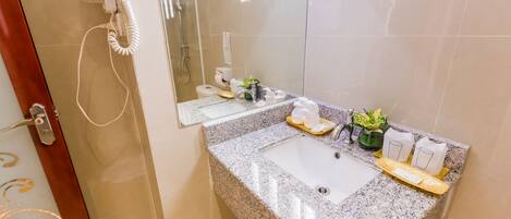 A bathroom with a granite countertop, a white sink, a handheld hair dryer, and a potted plant.