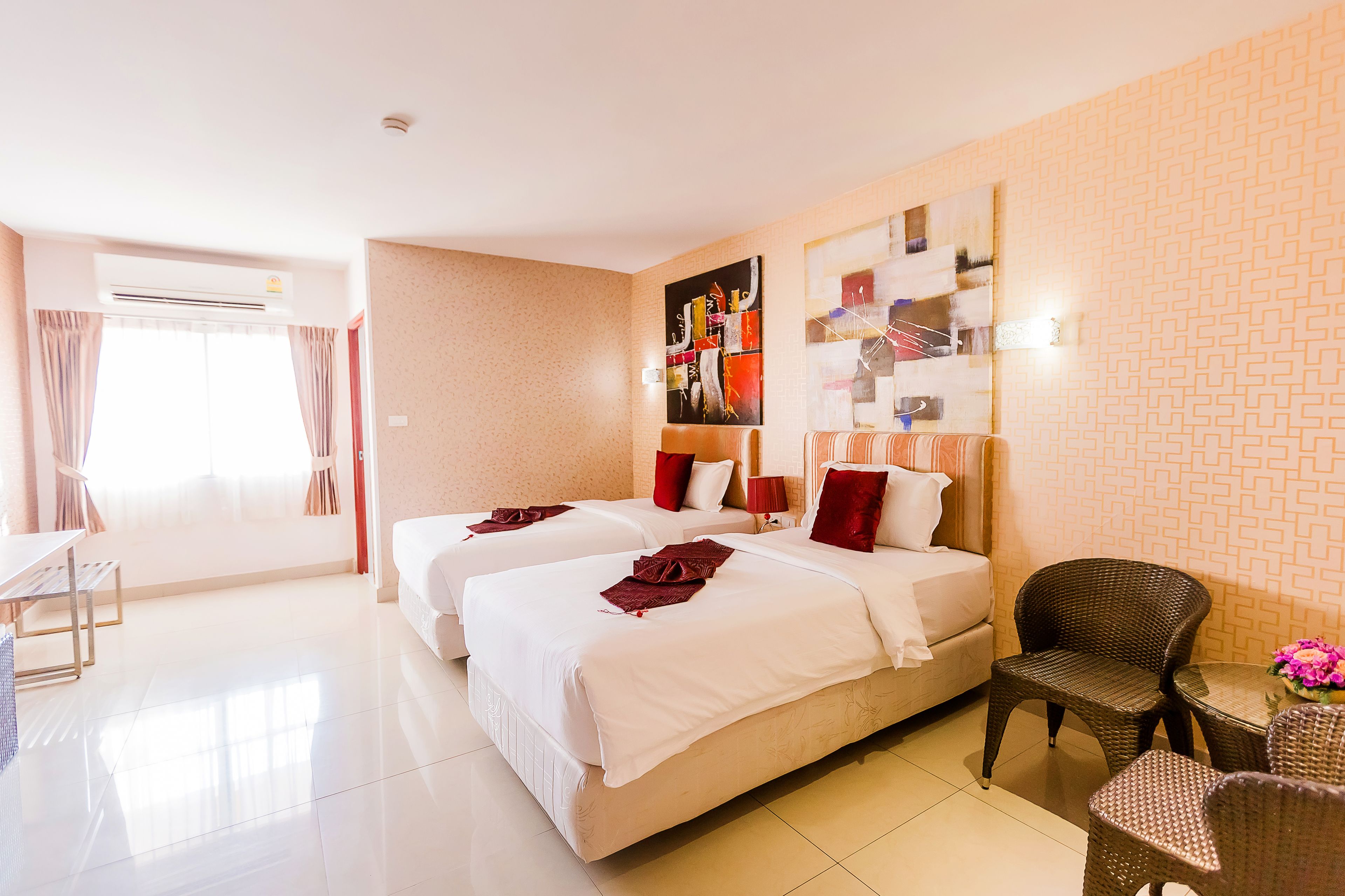 A hotel room with two beds, a dining table, and a wicker chair.