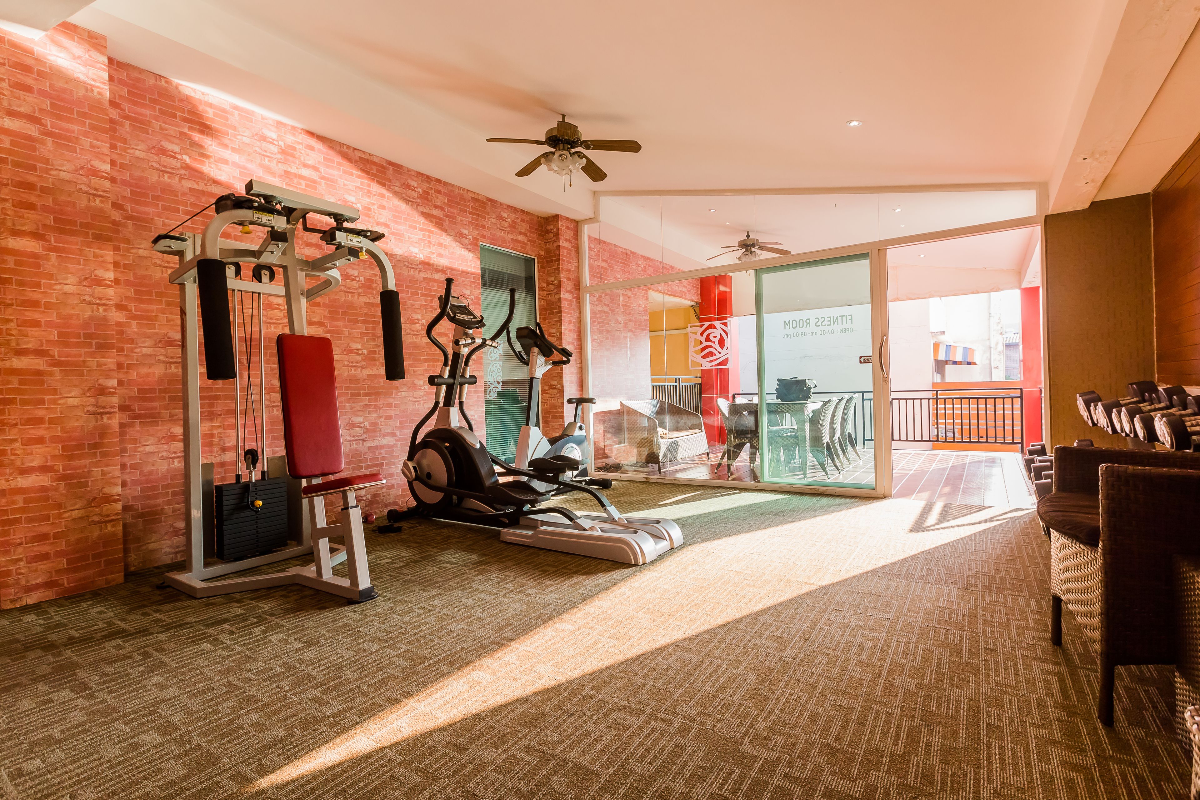 A gym with exercise equipment, a red wall, and a ceiling fan.