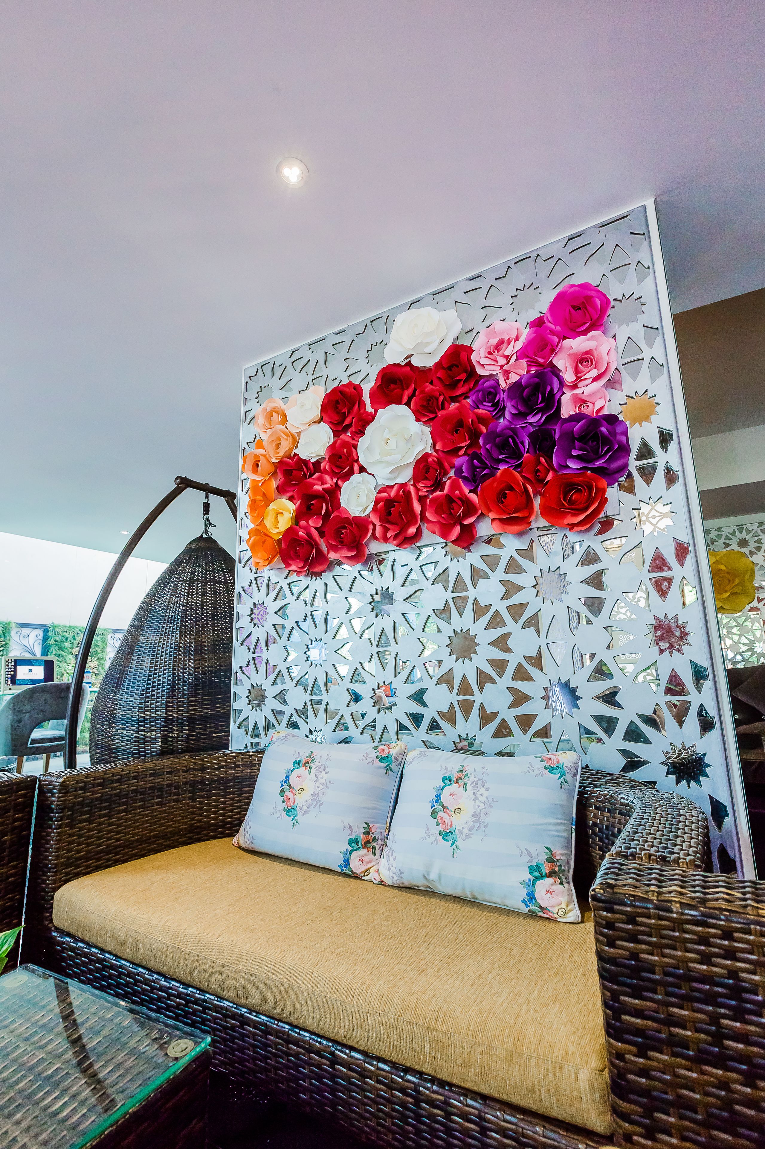 Un sofá de mimbre con cojines, un sillón colgante y una pared decorativa con diseños recortados.