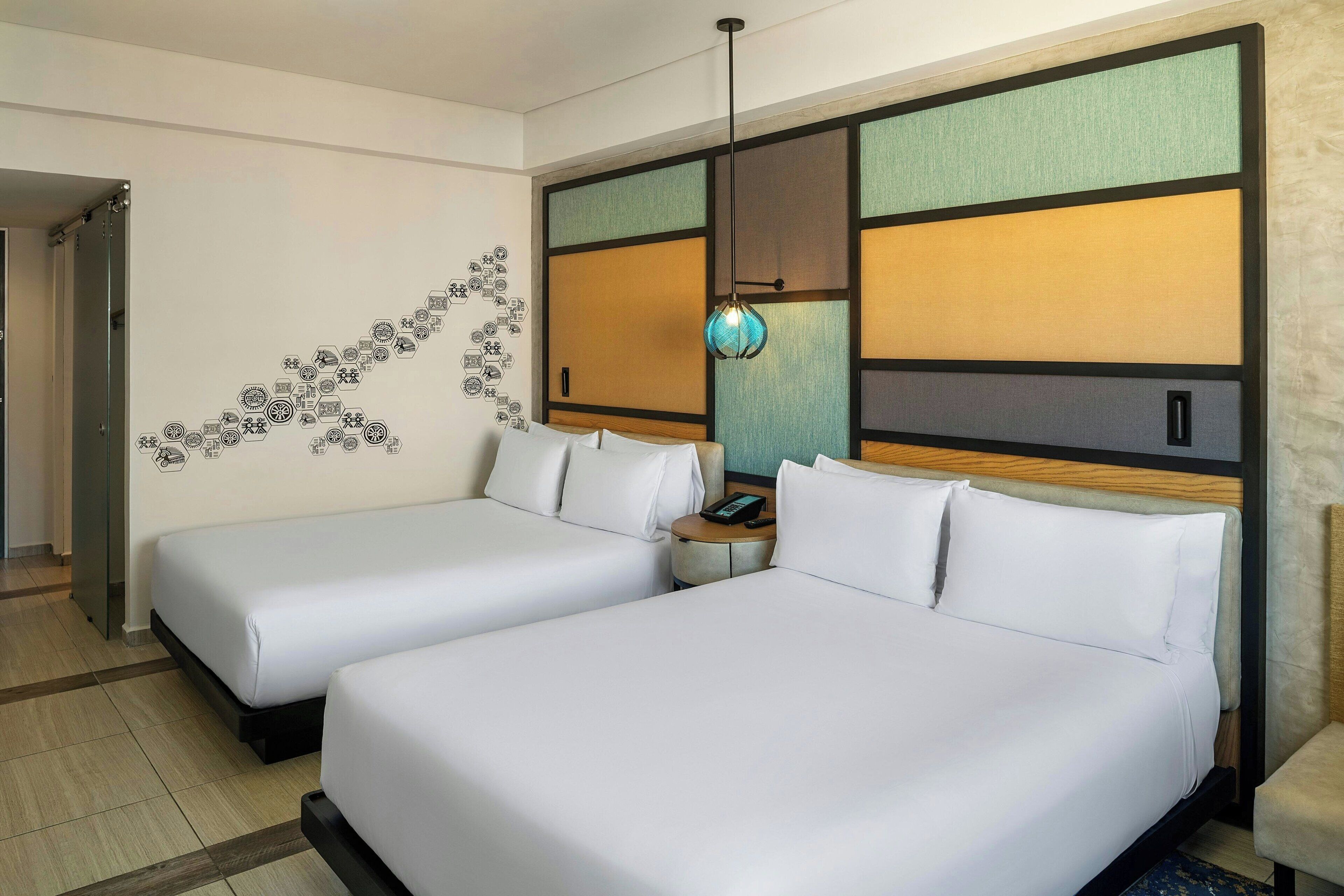 Una habitación de hotel con dos camas, una pared con diseños hexagonales, una lámpara colgante y un cabecero de madera.