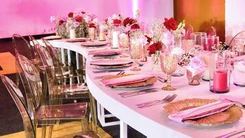 Una larga mesa dispuesta para un evento formal, con sillas traslúcidas, centros de mesa florales y vajilla elegante.