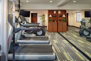 Un gimnasio con cintas de correr, un espejo, dispensador de agua y un reloj.