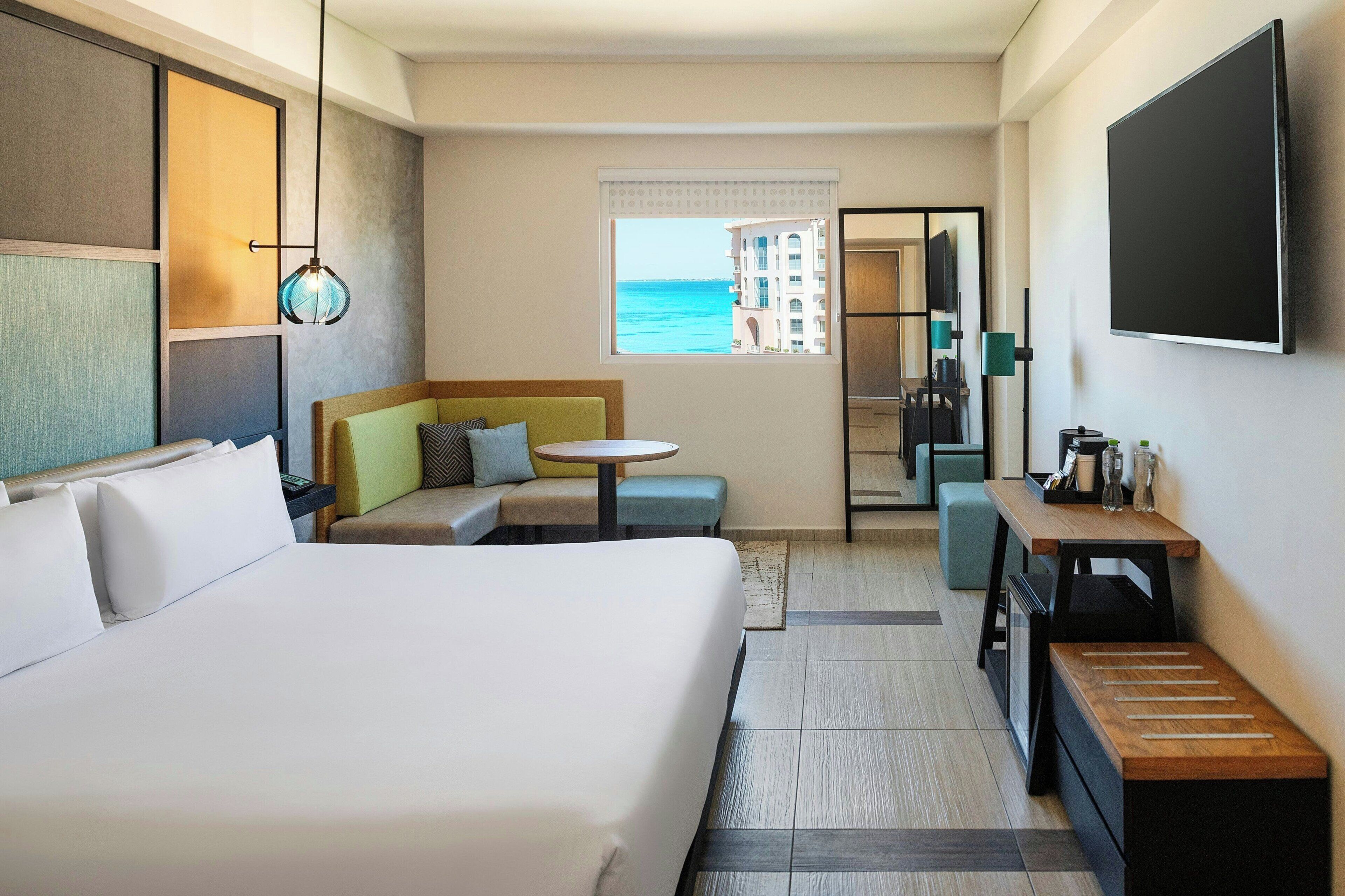 Une chambre d’hôtel avec un grand lit, un coin salon avec vue sur la mer, une petite table et un téléviseur fixé au mur.