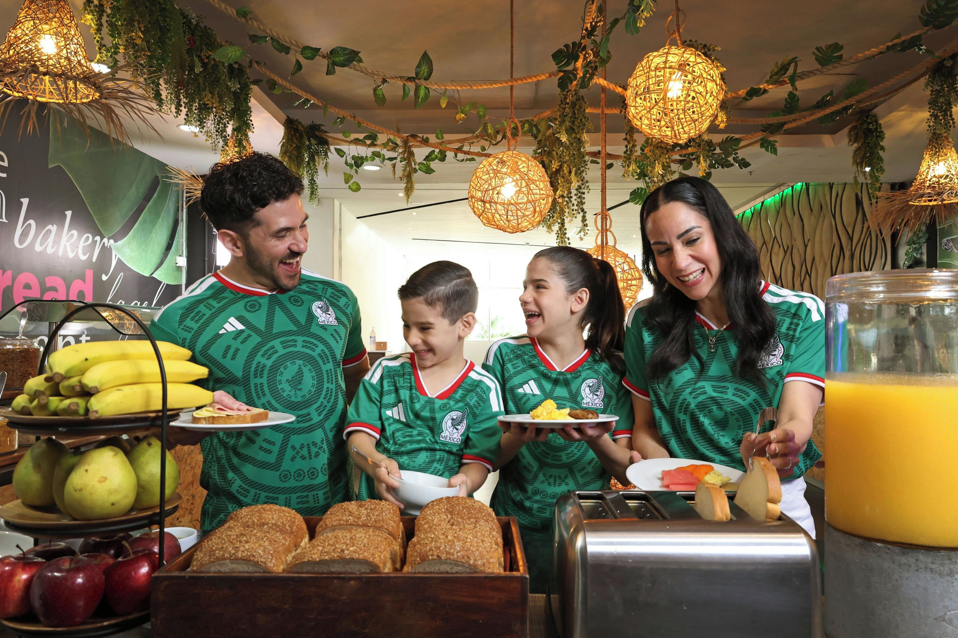 A group of people in a room with a buffet table featuring bread, fruits, and a juice dispenser.
