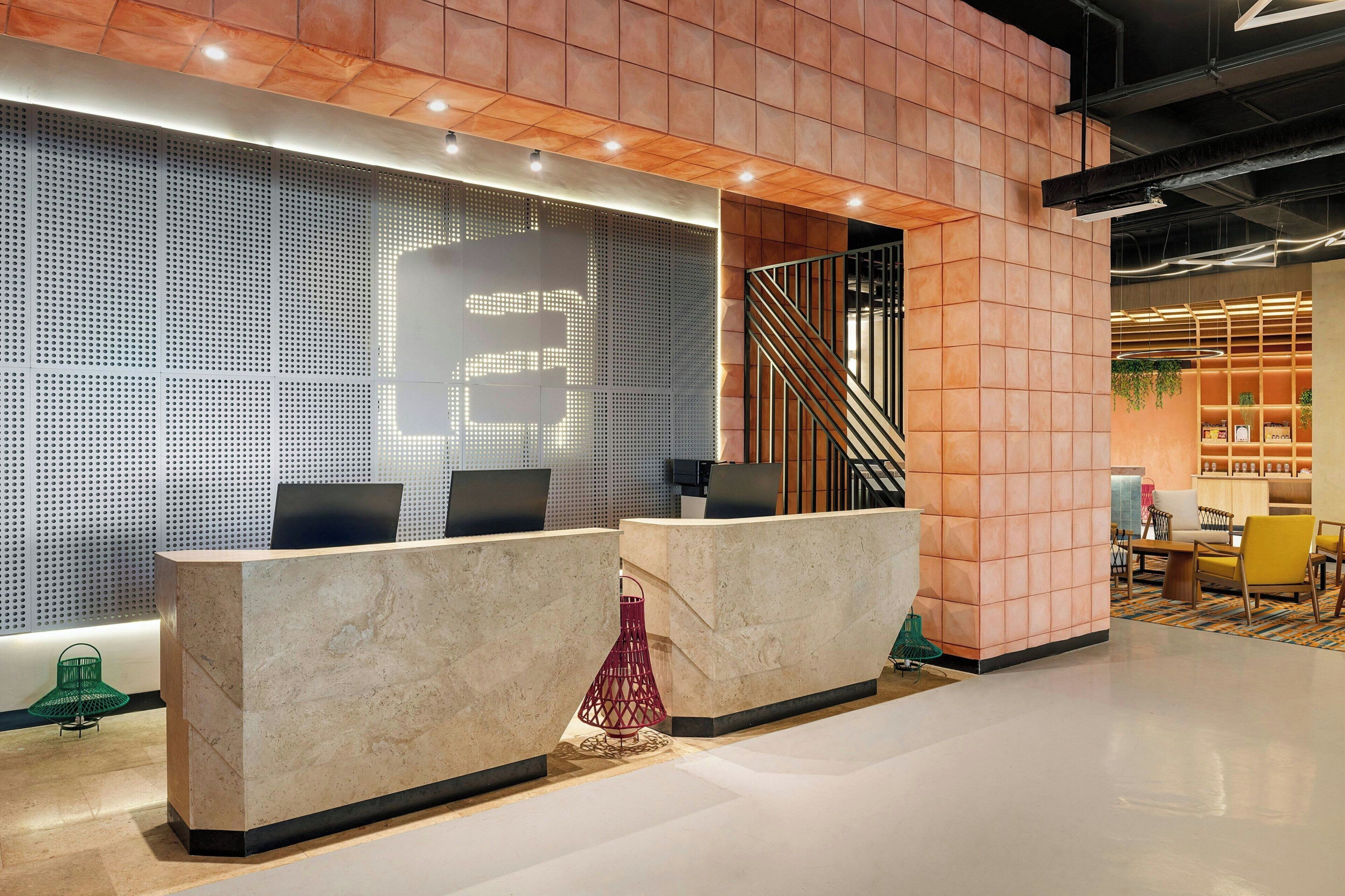 A modern reception area with a marble counter, a digital display, and a staircase leading to an upper level.