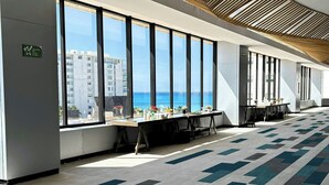A spacious hotel lobby with large windows offering ocean views, a patterned carpet, and a modern ceiling design.