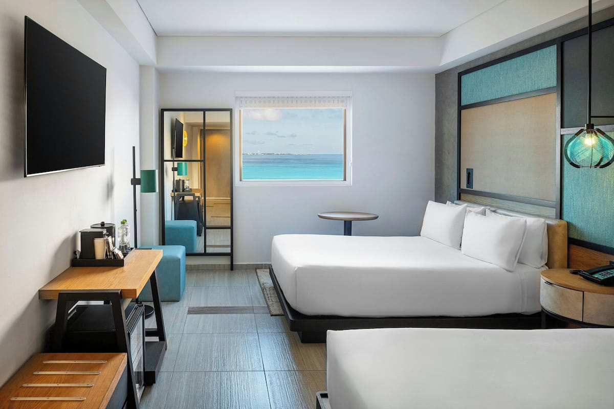Habitación de hotel con una cama grande, un escritorio, una mesita y vistas al mar a través de una ventana.