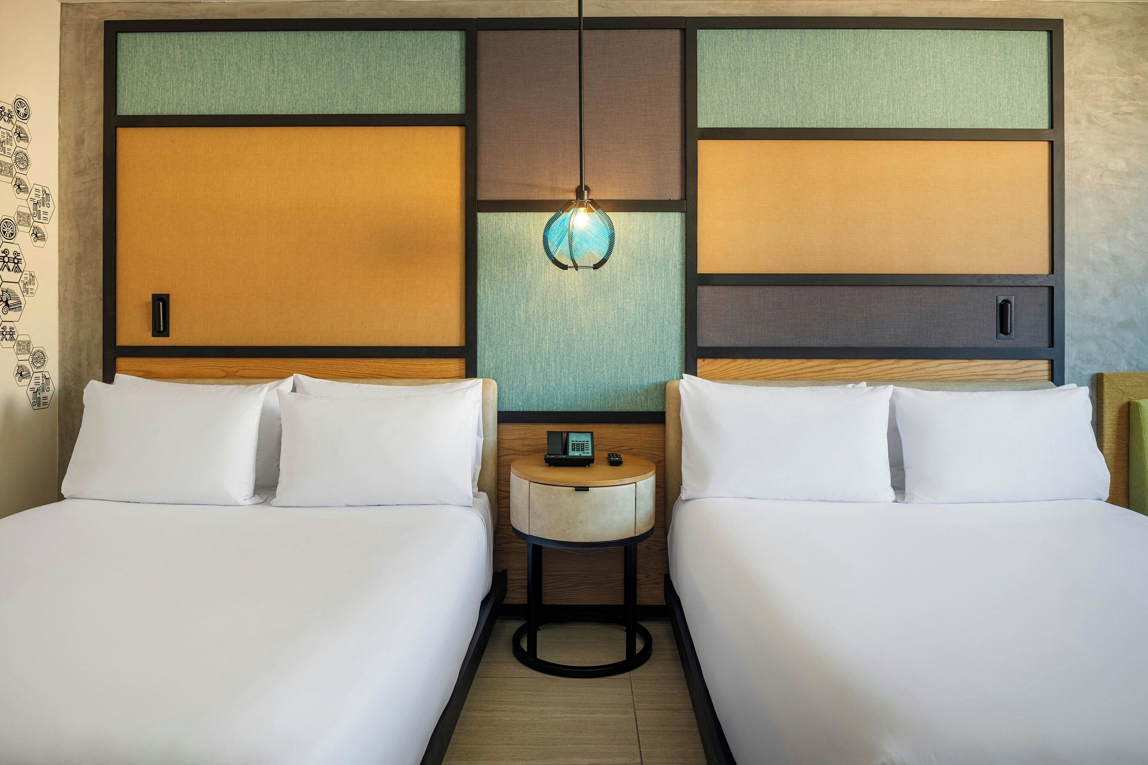 A hotel room with two beds, a small bedside table with a phone, and a wall with a geometric design.