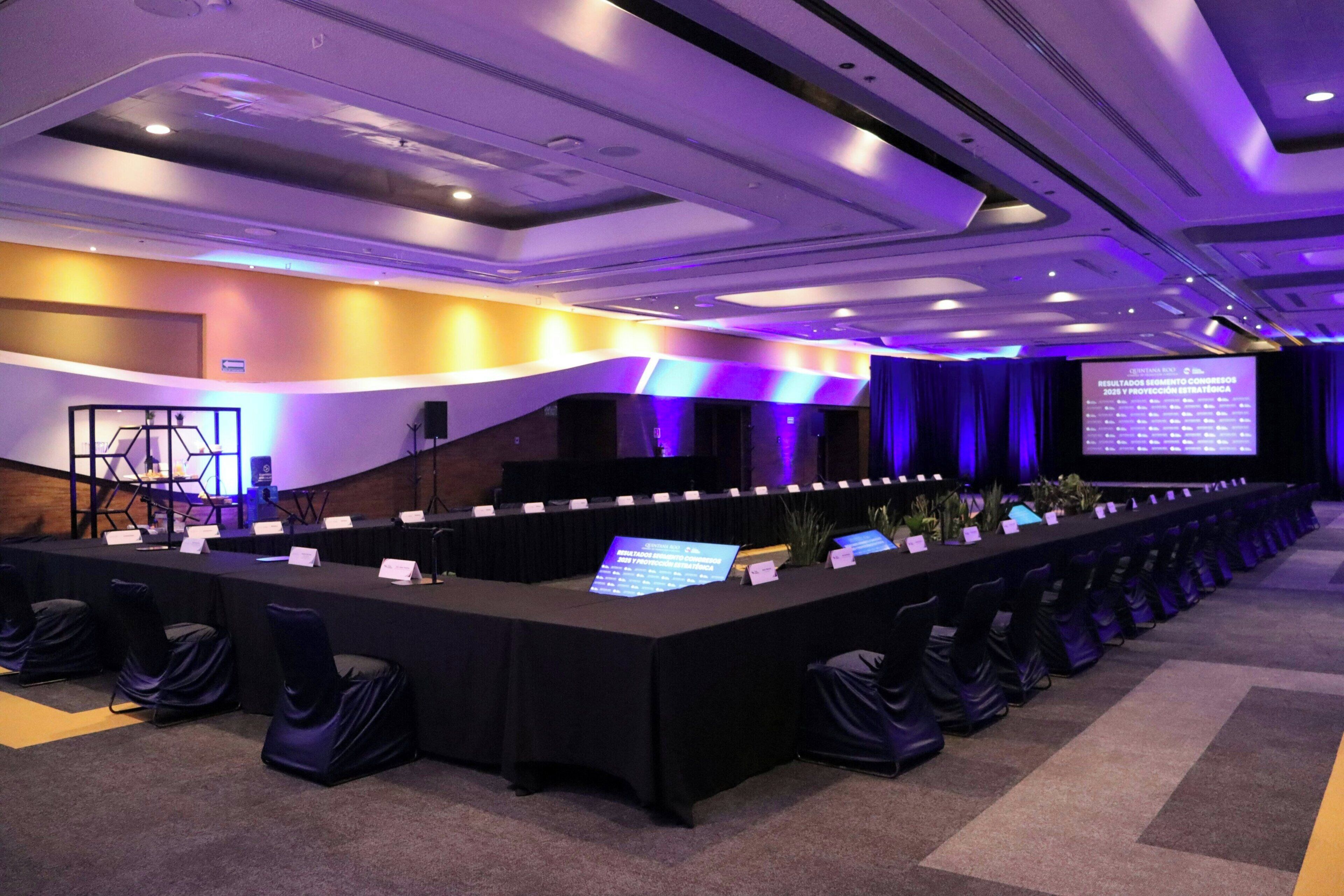A conference room with a long table, chairs, a projector screen, and a stage.