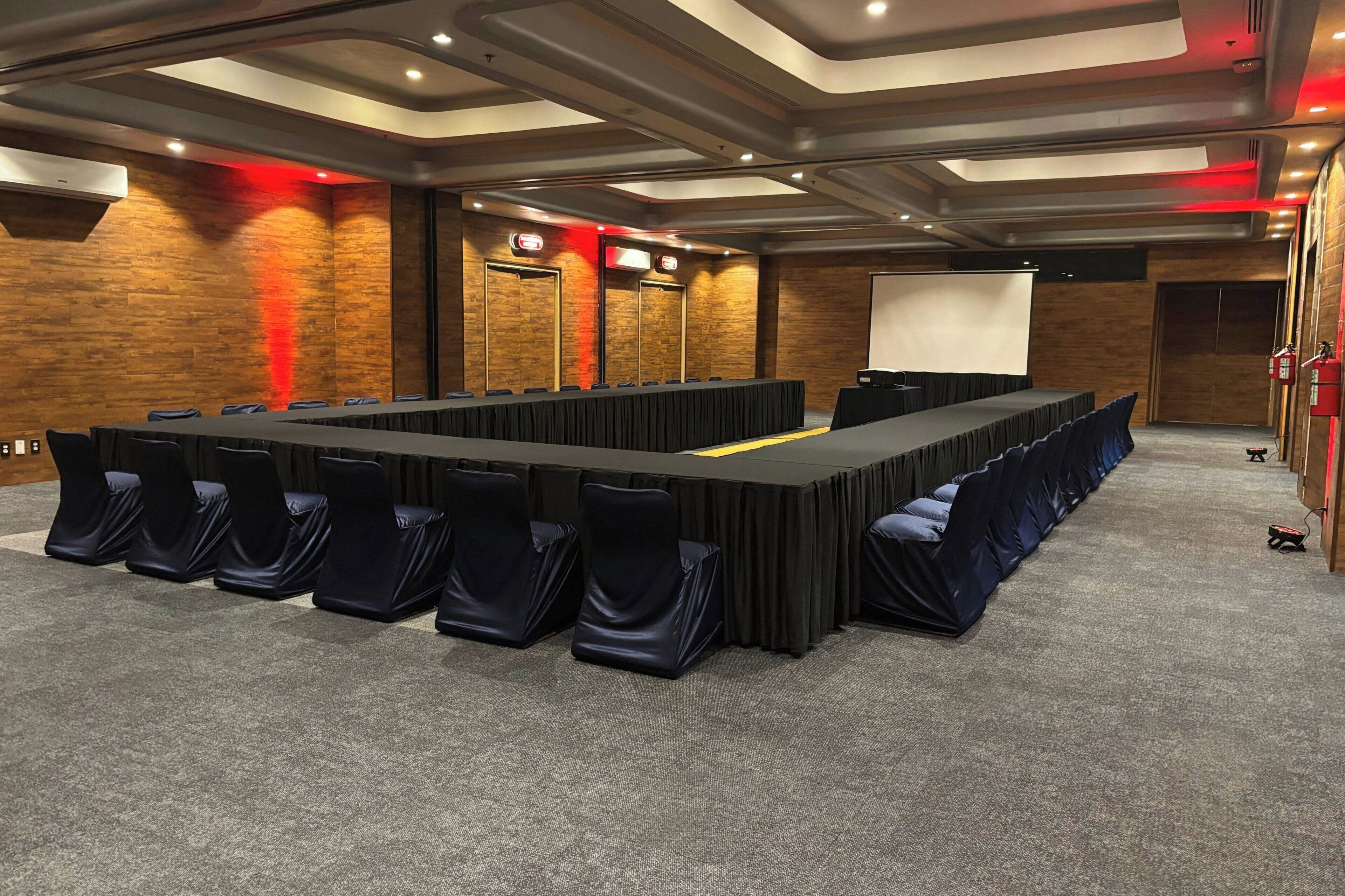 A conference room with a long table, chairs, a projector screen, and a fire extinguisher.