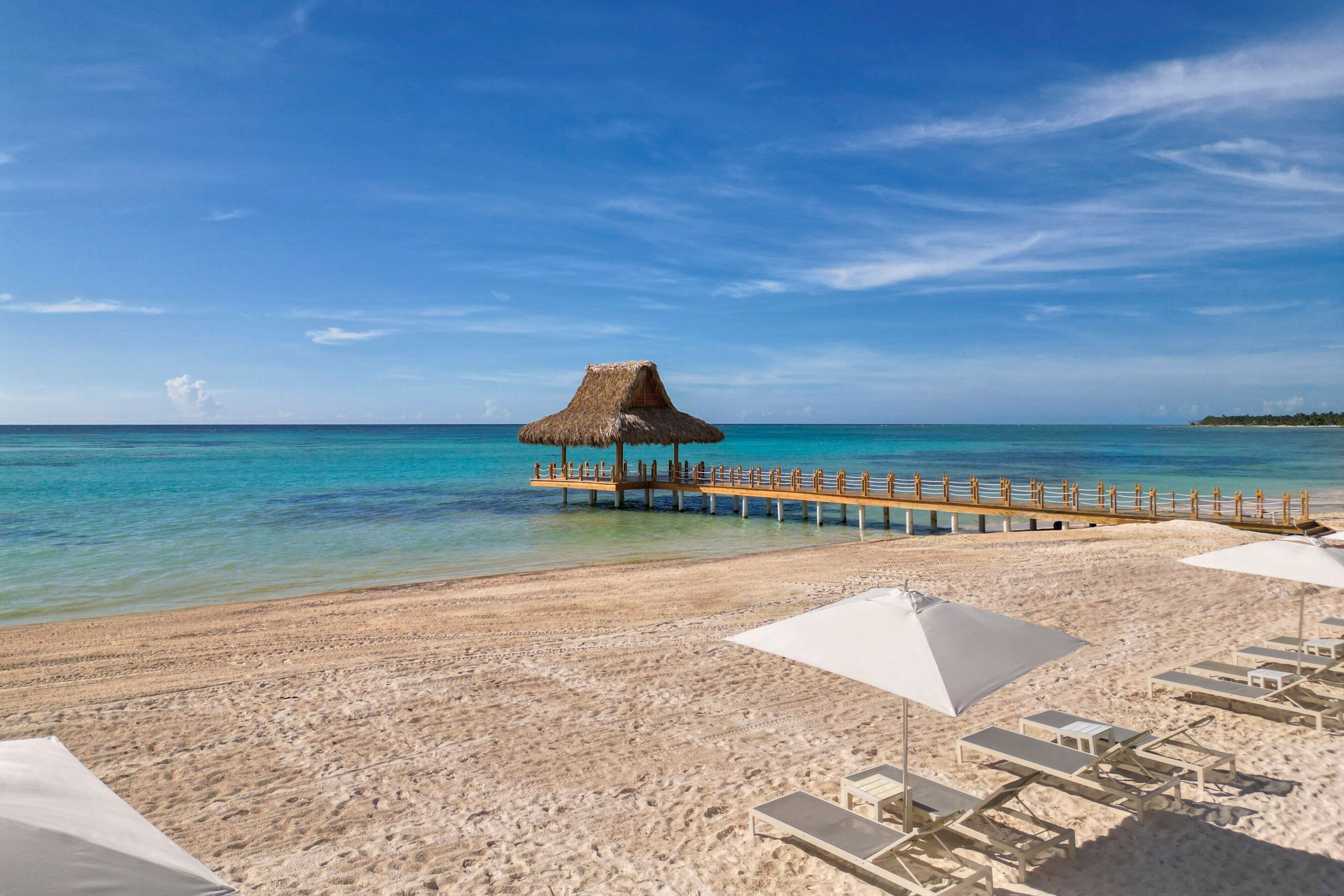 Ein Strand mit weißen Sonnenschirmen, Liegestühlen und einer Strandhütte auf einem Steg.